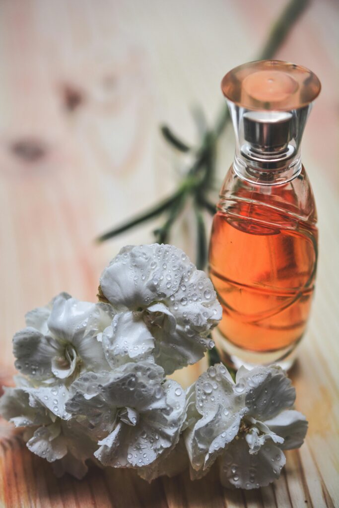 pexels-photo-264950-264950 Glass perfume bottle alongside dew-kissed white carnation flowers on wood surface.